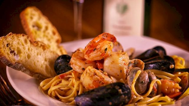 A plate of spaghetti with mussels and shrimp, topped with herbs, with garlic bread on the side.